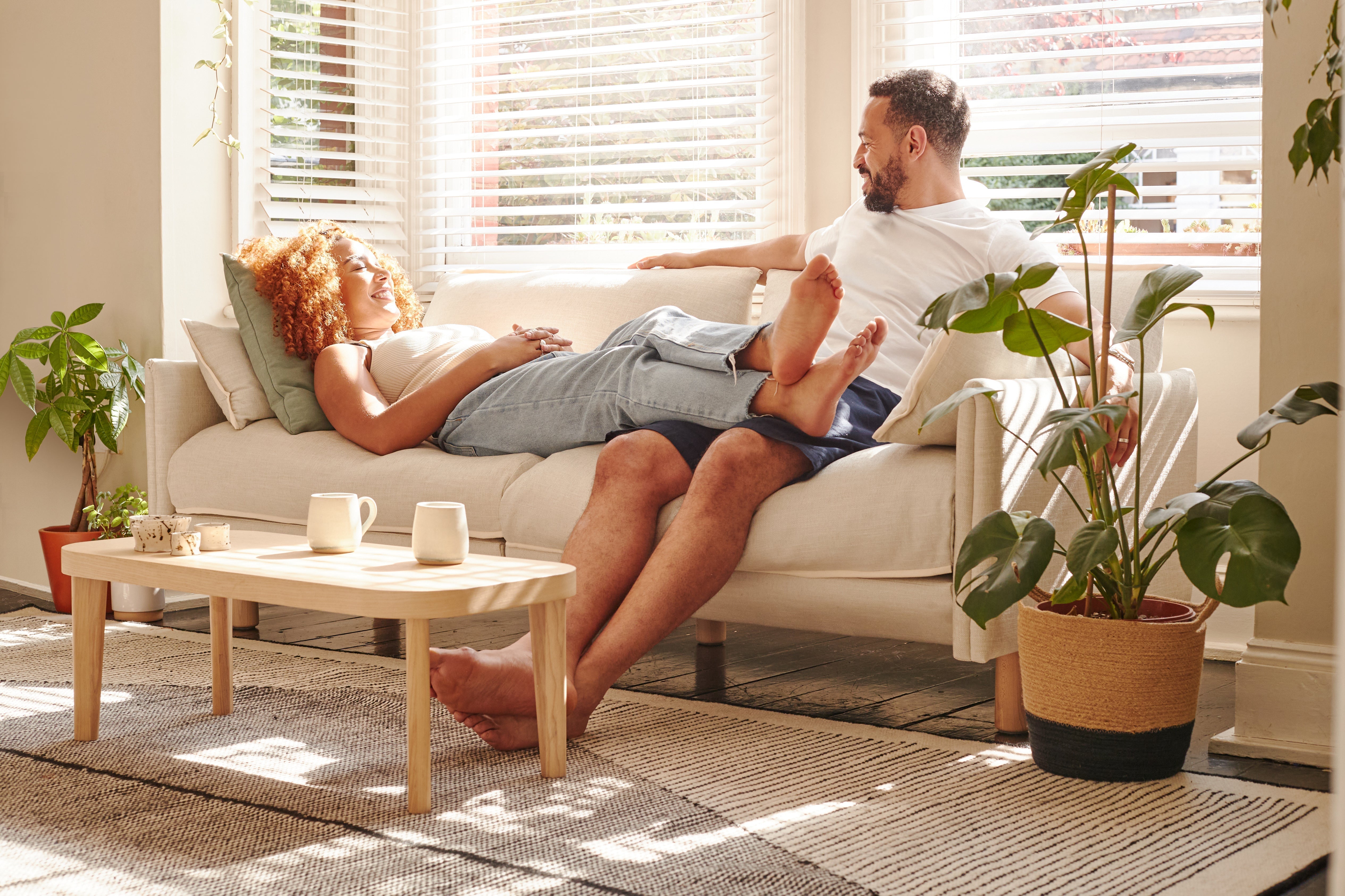 Couple relaxing on a cream fabric sofa in a sunlit living room with warm neutral tones, natural textures and soft spring colour accents.