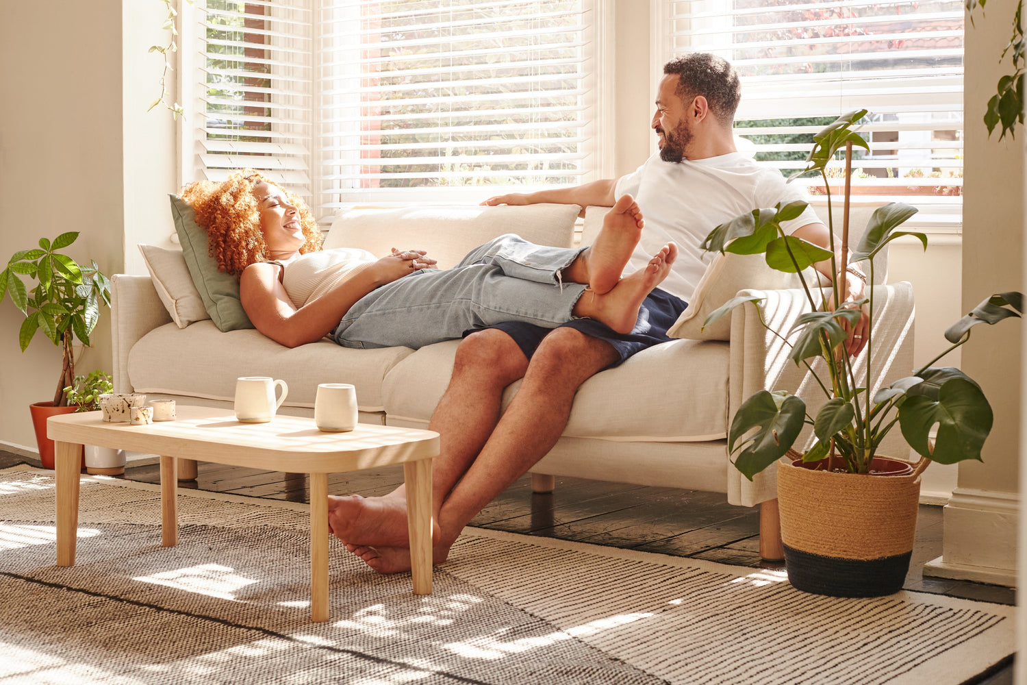 Couple relaxing on a cream fabric sofa in a sunlit living room with warm neutral tones, natural textures and soft spring colour accents.